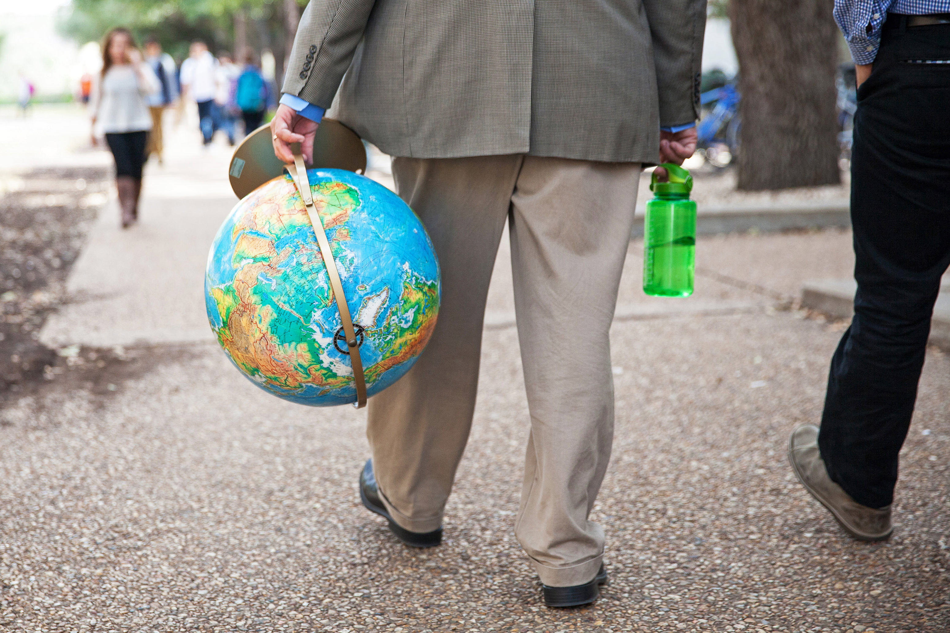 A professor walks through campus holding a globe